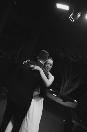 Black and white photo of a bride and groom sharing their first dance at a wedding reception under stage lighting.