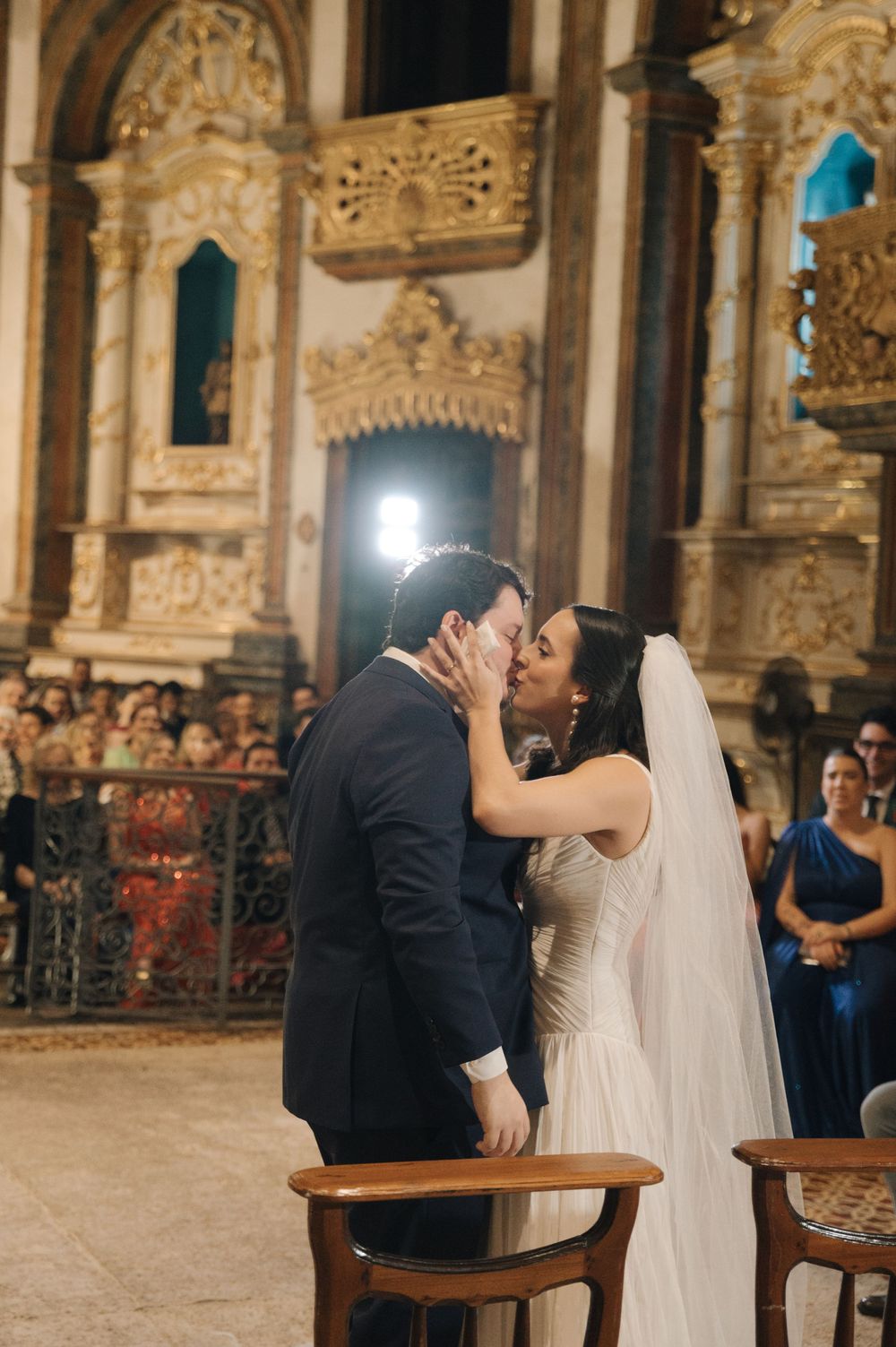 A romantic wedding kiss in an ornate church with golden baroque details and stone columns.