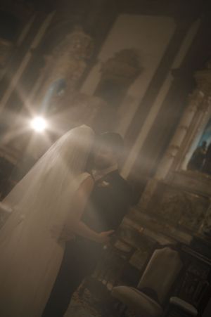 A romantic first dance between newlyweds in a dimly lit ballroom with ethereal light beams streaming through the haze.