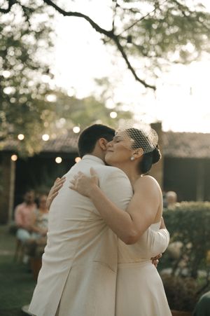 A romantic wedding couple embraces outdoors during a garden ceremony with soft bokeh lighting in the background.