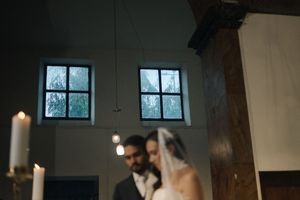 Bride and groom stand at the altar during a wedding ceremony in a dimly lit chapel with candlelight.