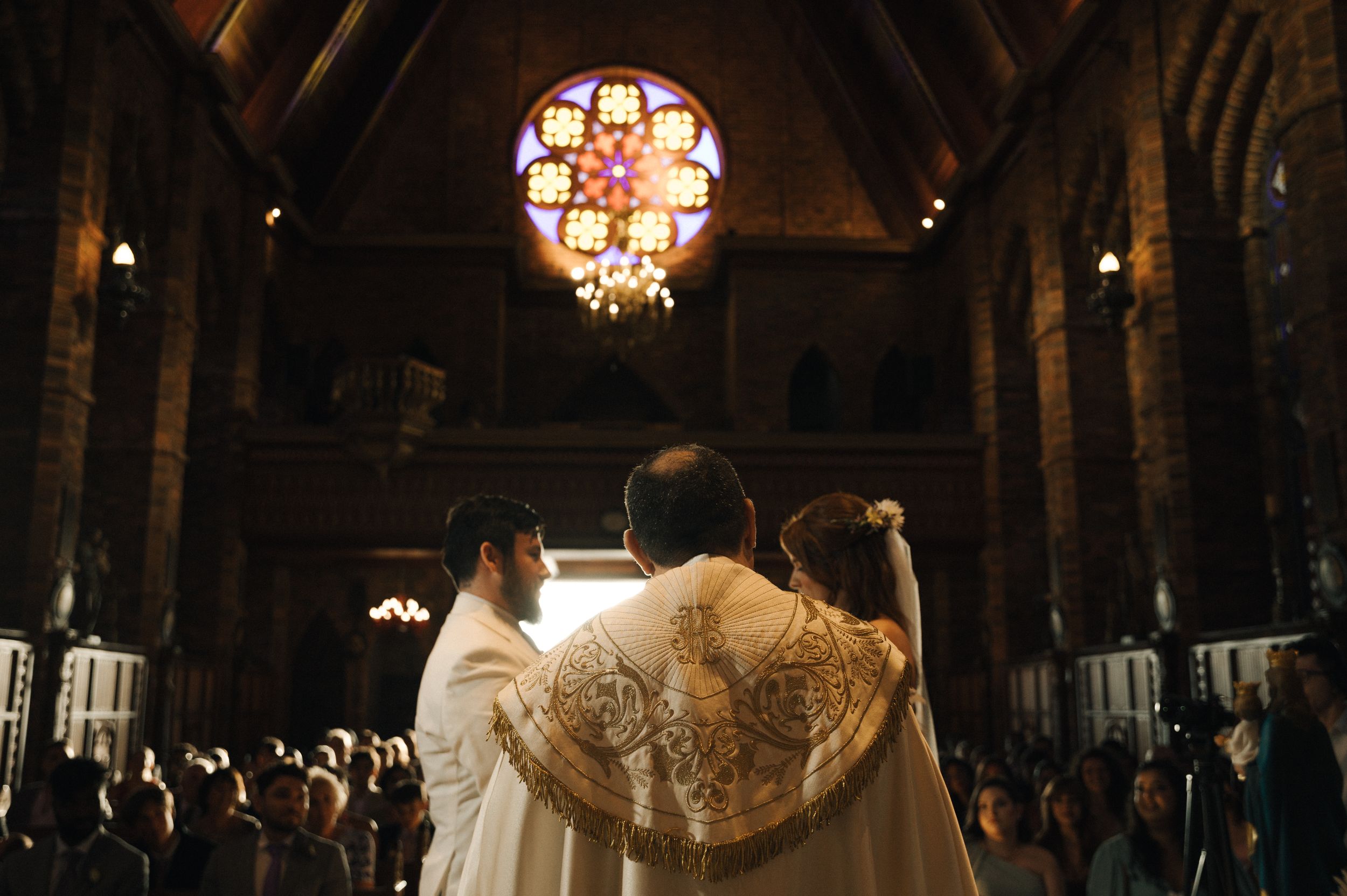 Elegant wedding reception venue with ornate chandeliers and guests seated at long tables in a dimly lit room.
