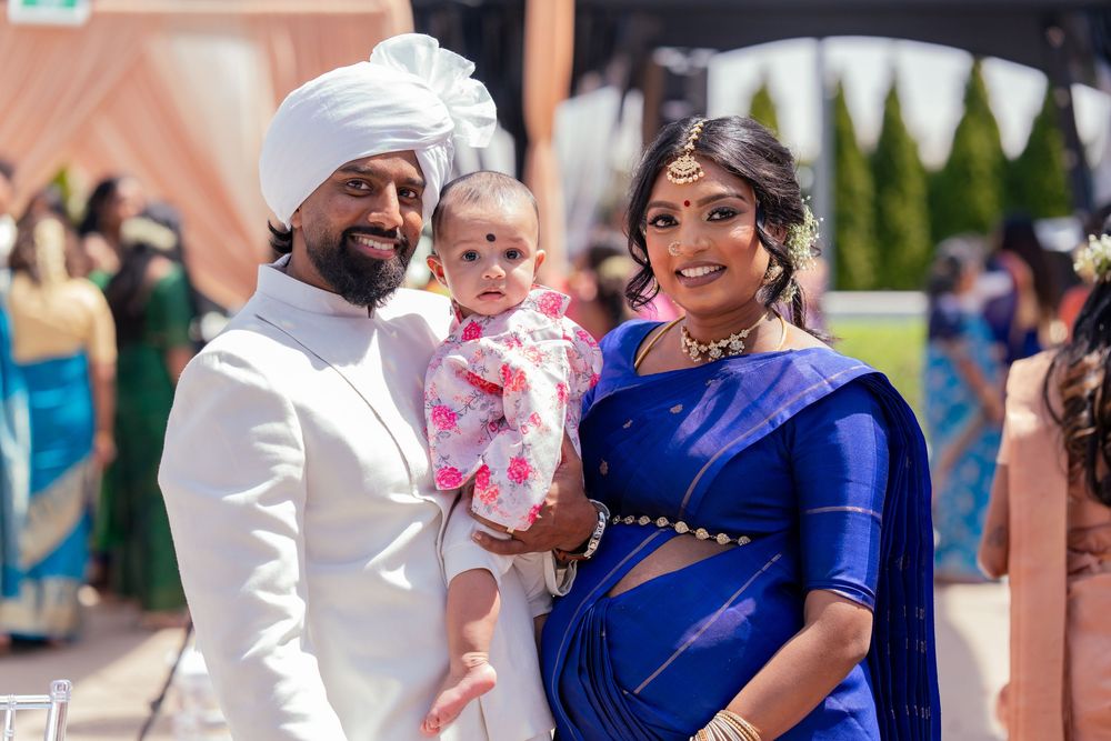 Family in traditional South Asian attire with baby wearing pink at outdoor celebration.