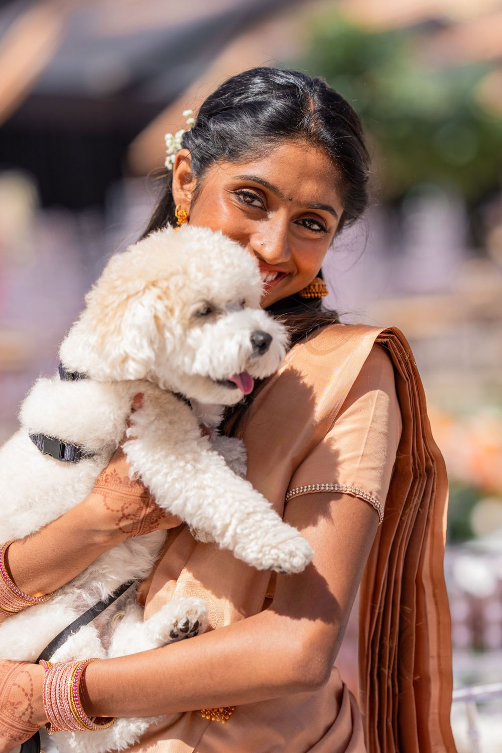 Woman in peach saree holding and cuddling a small white fluffy dog.