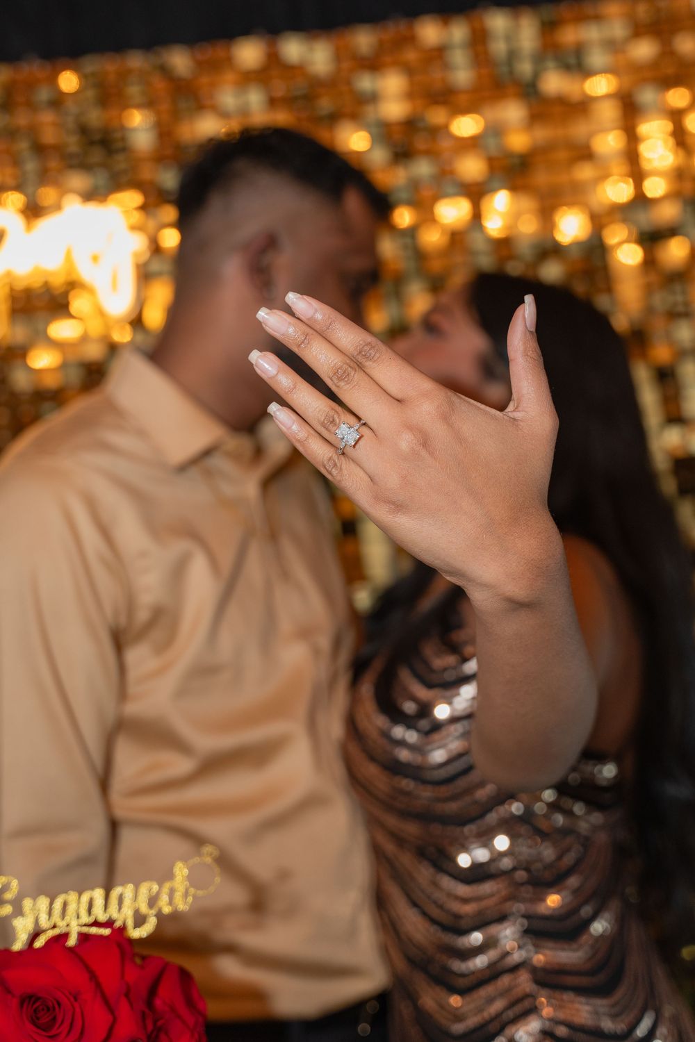 Engagement ring sparkles as couple shares intimate moment against golden bokeh background.