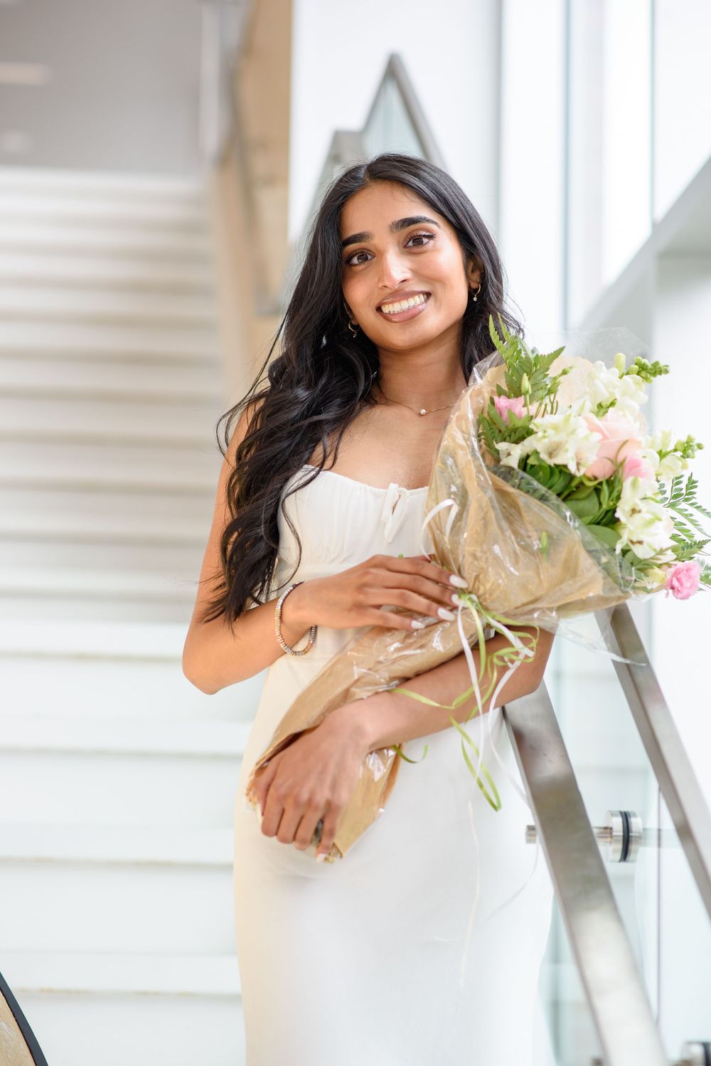 Graduate holding beautiful bouquet of pink and white flowers on staircase.