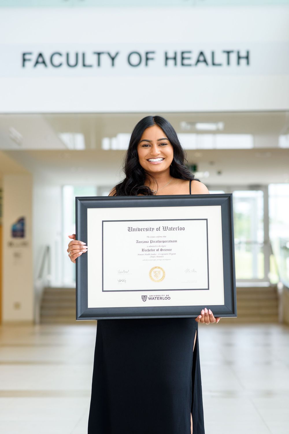 Graduate showing her new diploma in black frame at Faculty of Health foyer.