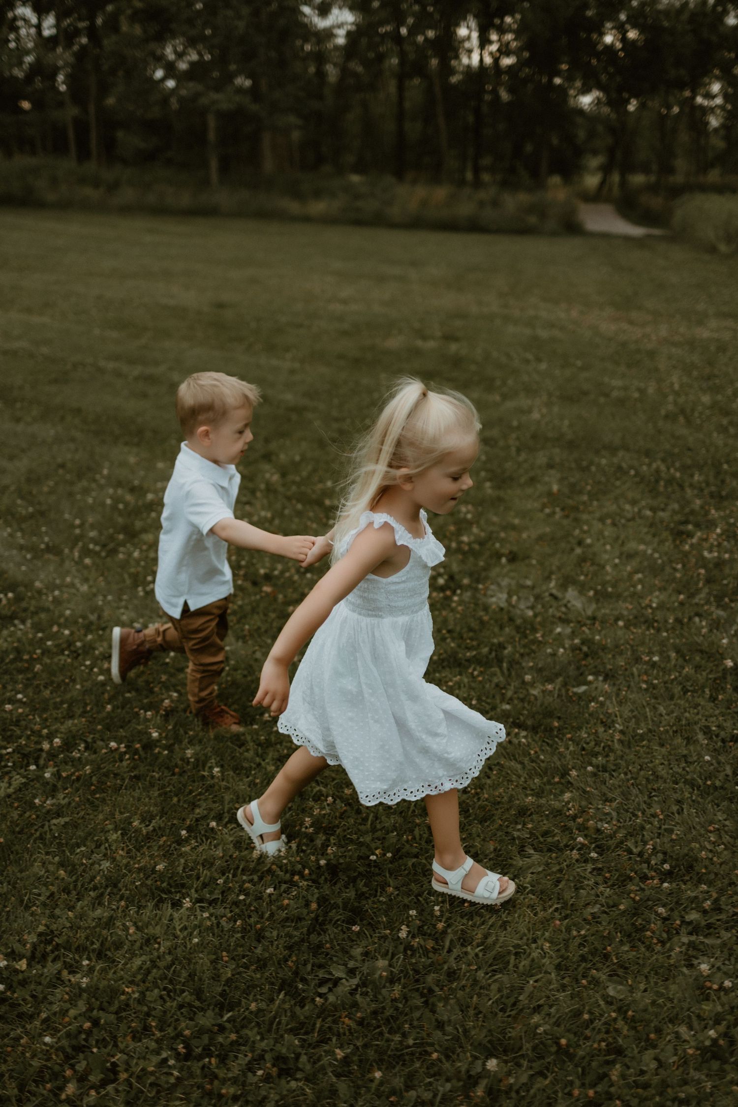 Two young children playing and running together in a grassy park on a summer day.