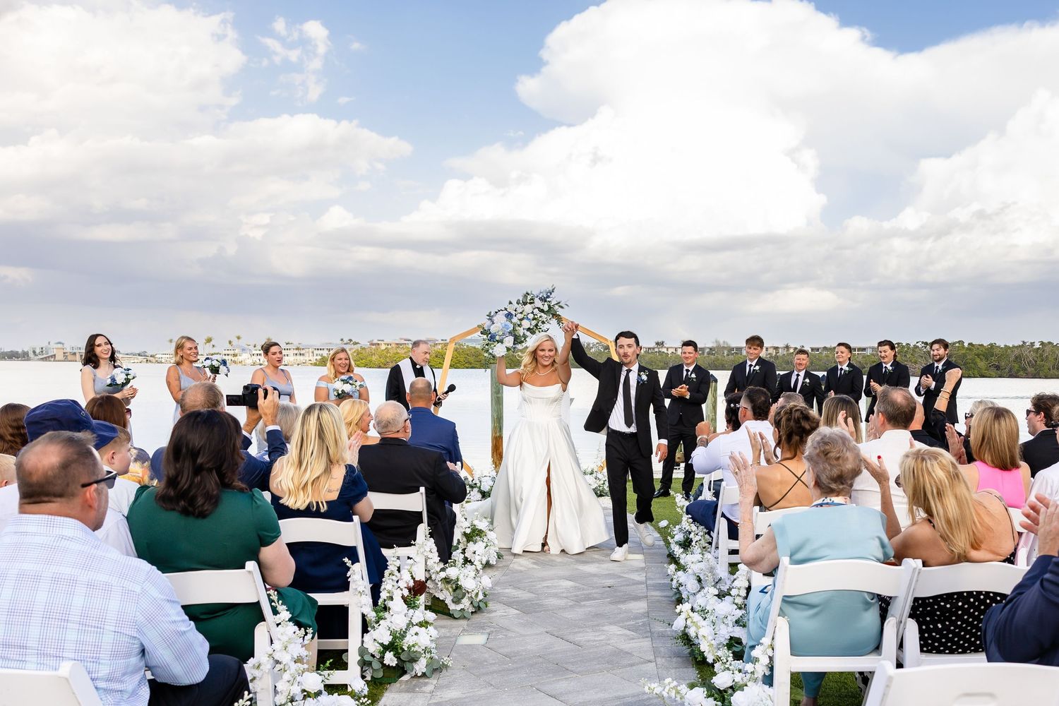 Bride in lace gown and groom in purple tuxedo pose before ocean mural at wedding.