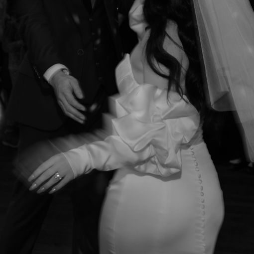 Close-up detail shot of a bride's wedding dress showing textured fabric and ruffled sleeve design.