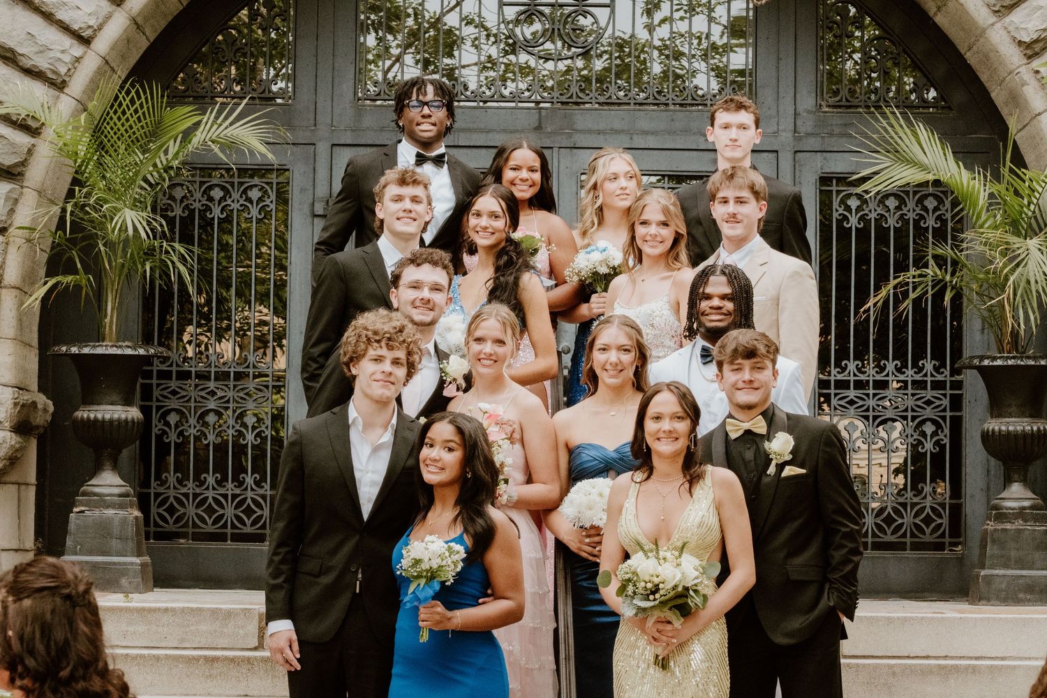 Large wedding party poses together in formal attire outside a grand venue.