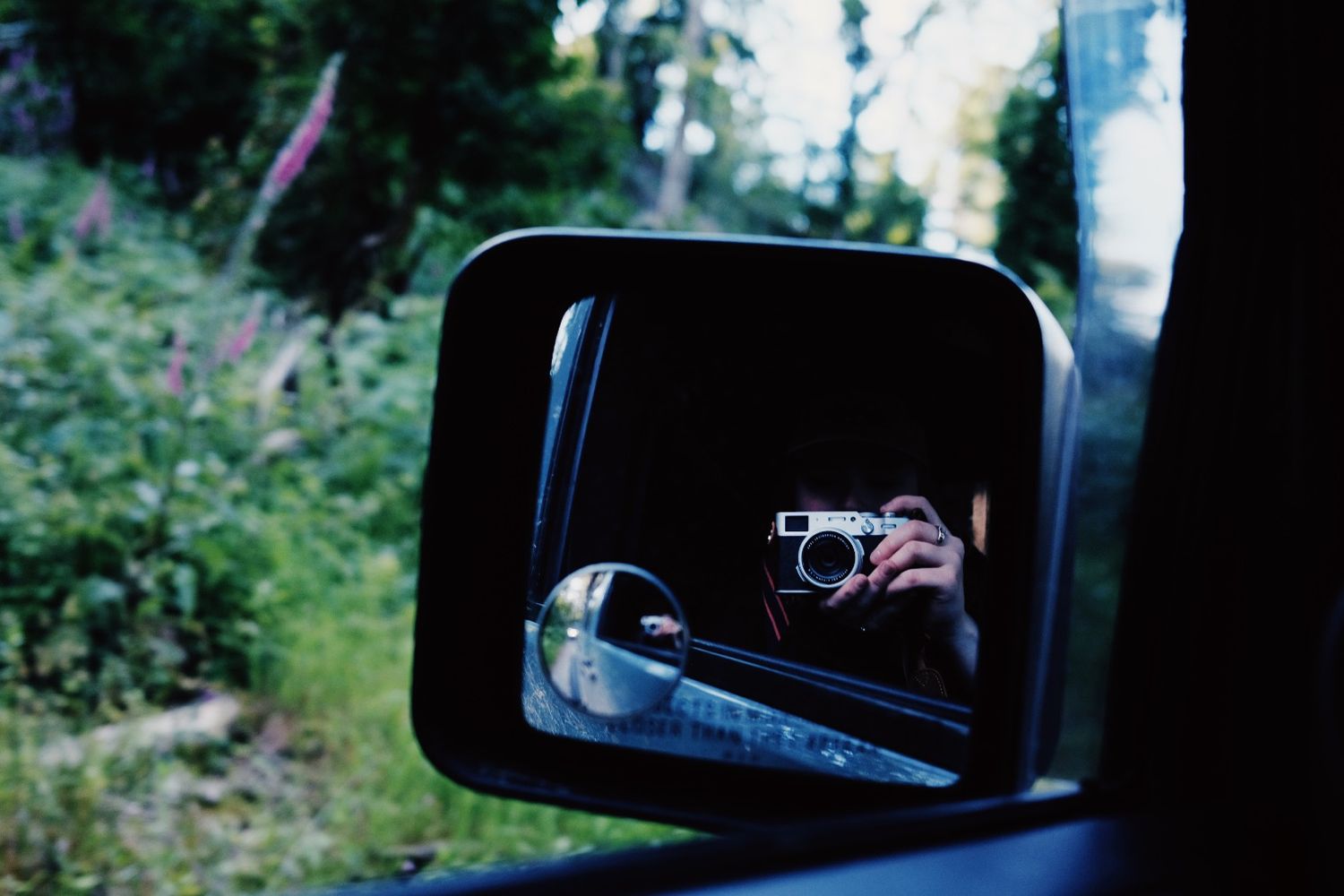 Car side mirrors and rearview mirror reflections in a forest setting.