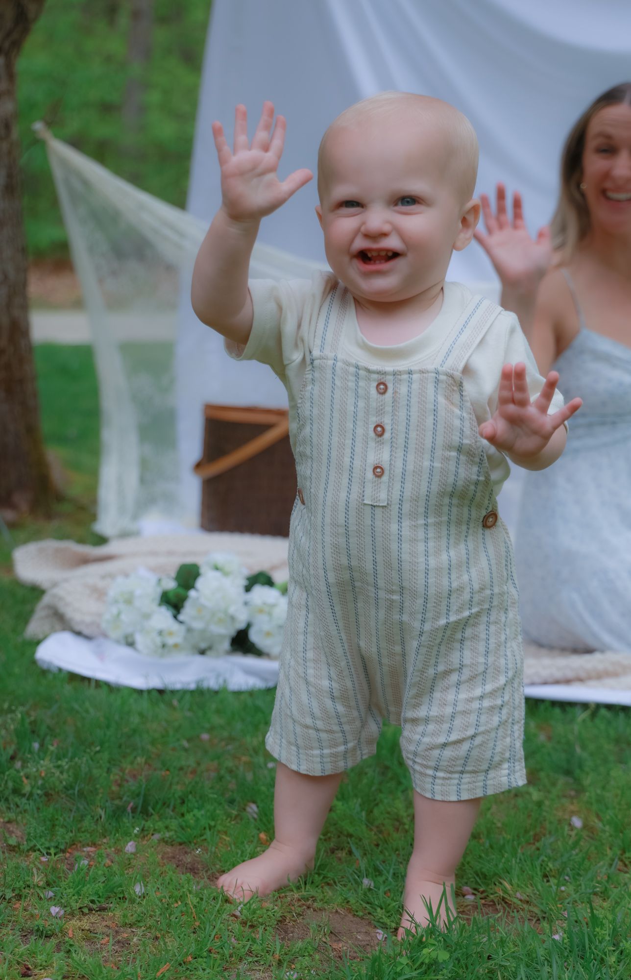 Baby in striped romper playing during outdoor photoshoot with white backdrop.