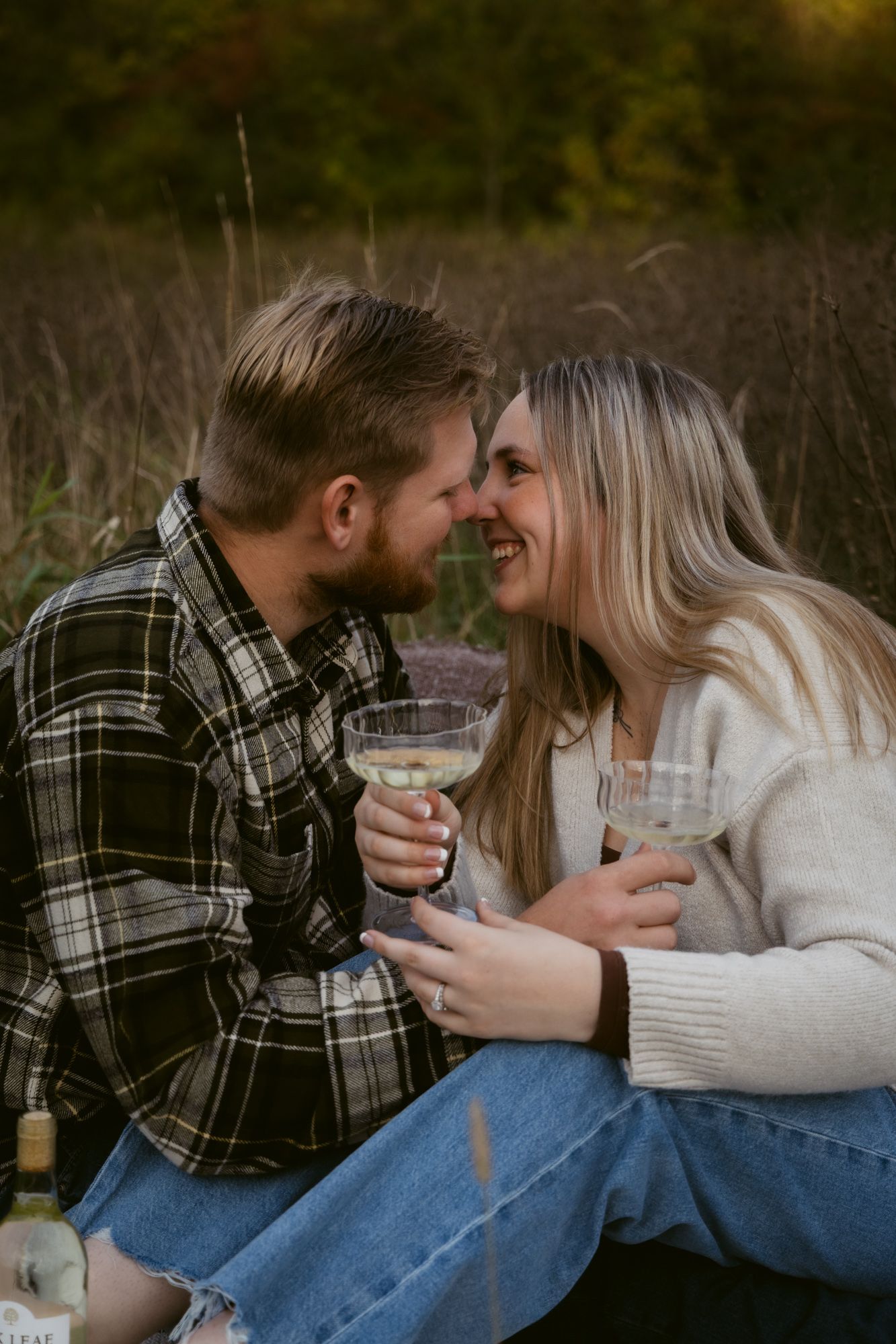 Romantic couple in casual attire sharing wine outdoors while sitting together on a cozy autumn afternoon.