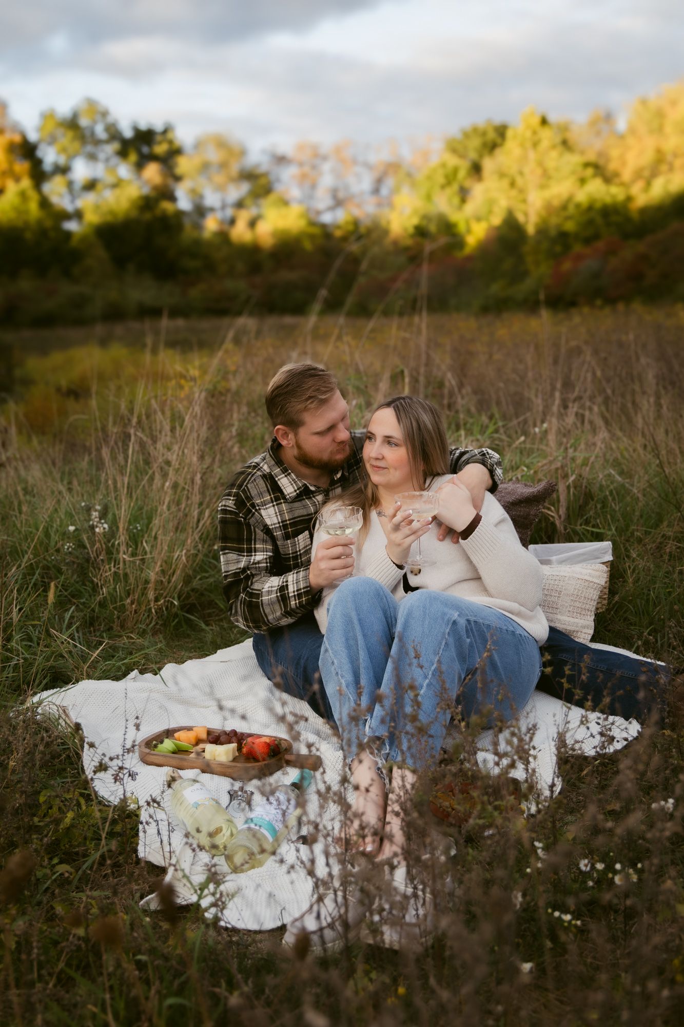 A couple enjoys a romantic fall picnic on a white blanket in a golden meadow at sunset.
