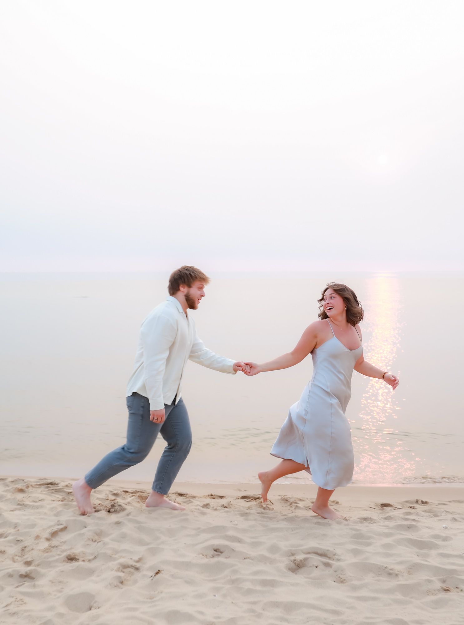 Playful couple running and chasing each other on beach sand at dusk.