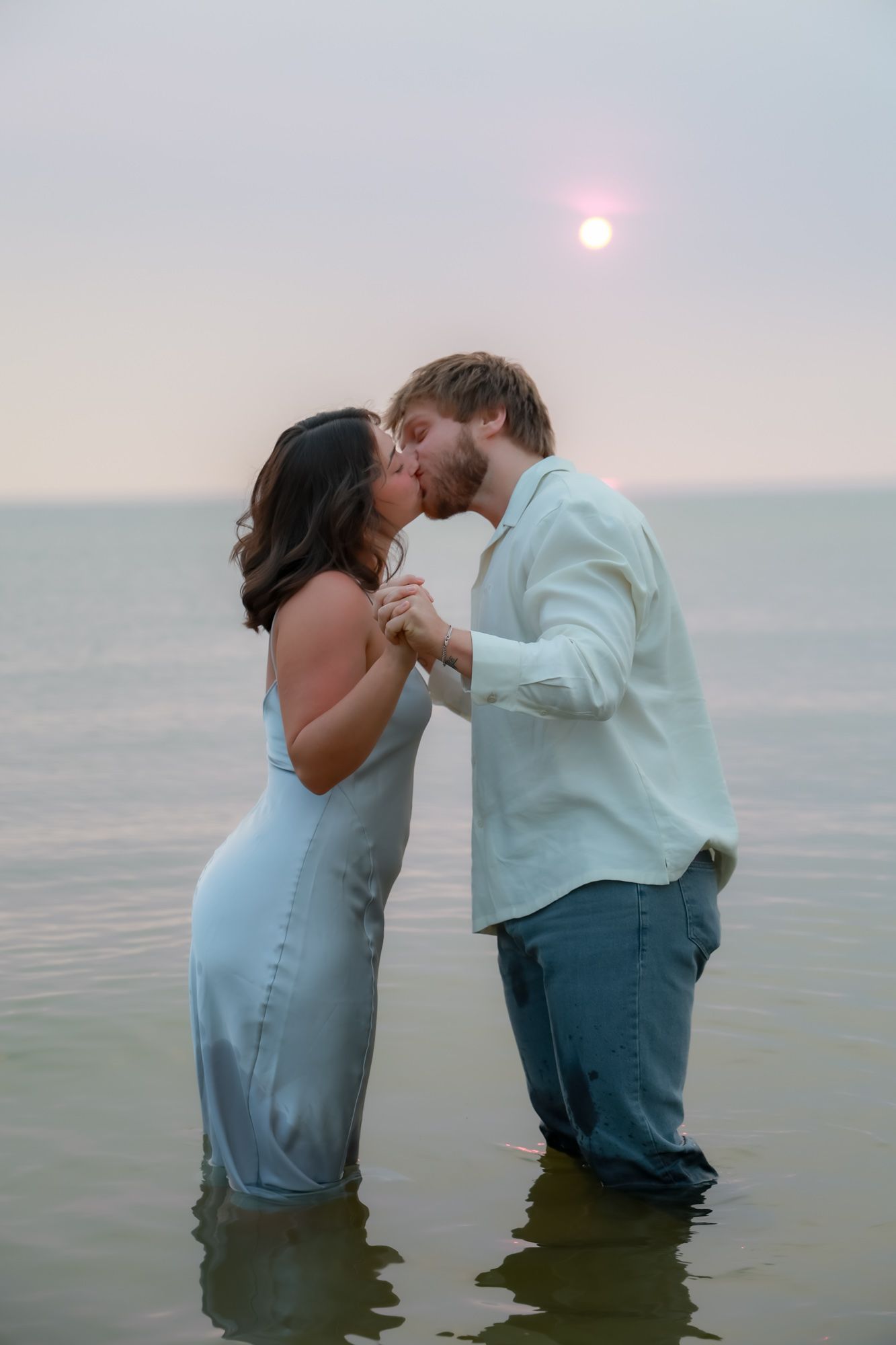 Couple sharing romantic moments while standing in ocean water at sunset.