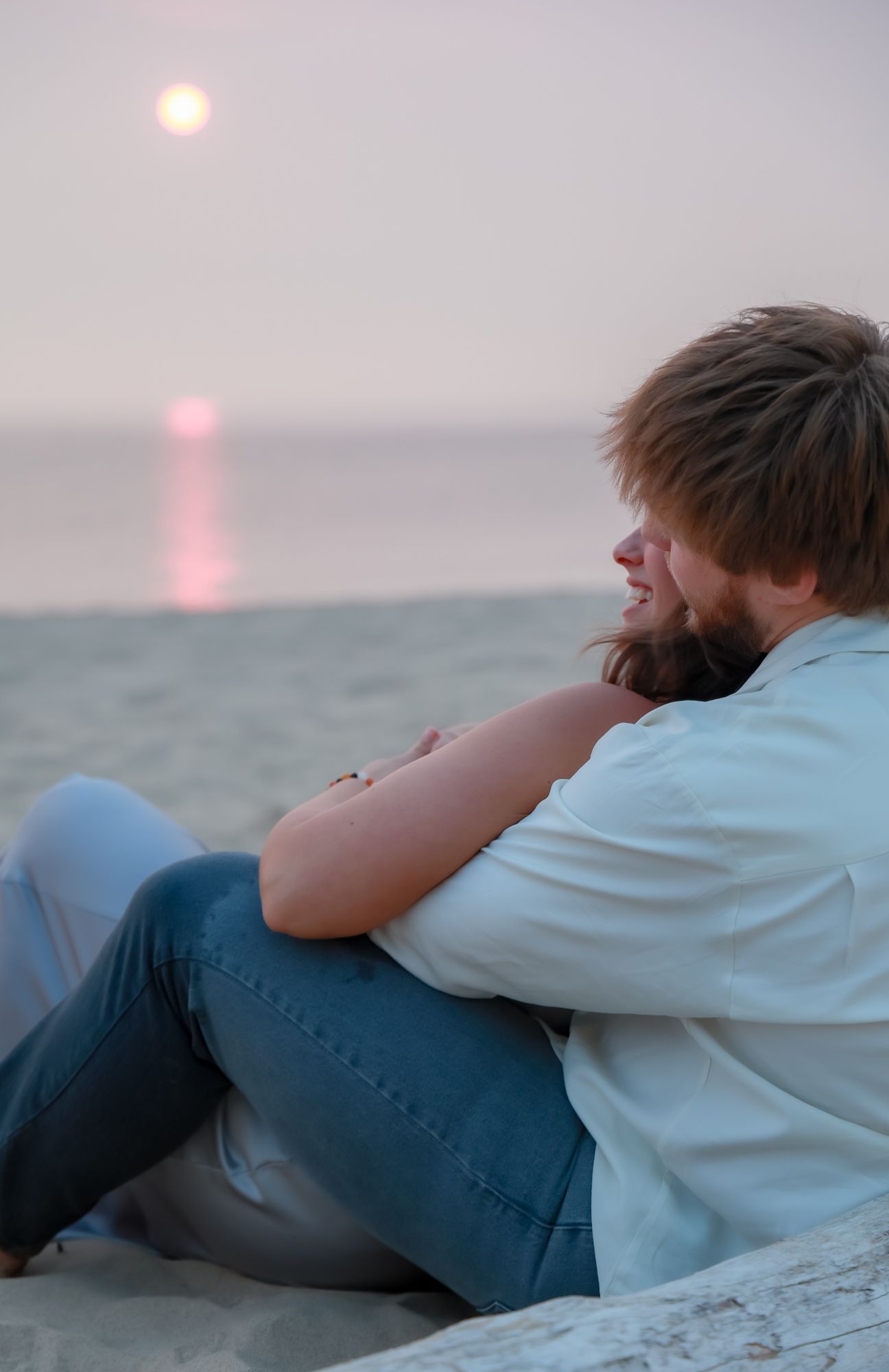 Couple resting peacefully together on beach with sunset over water in background.