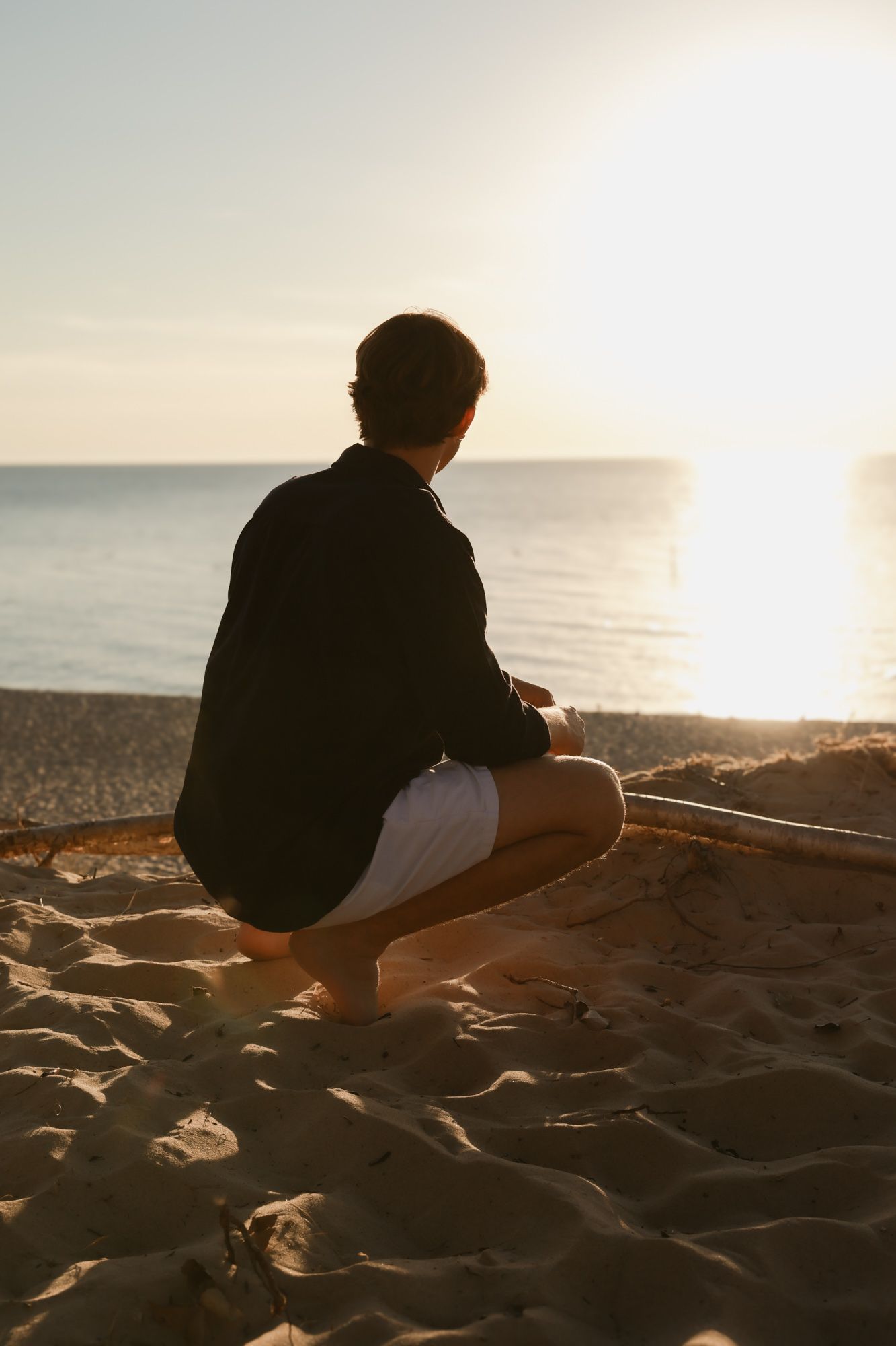 A silhouetted figure sits on a sandy beach at sunset, creating a peaceful seaside scene.