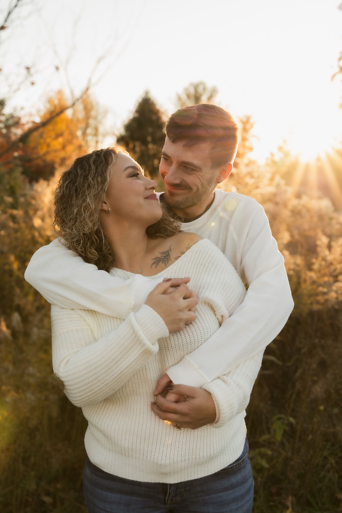 Couple in matching white sweaters share intimate moments during golden hour sunset photoshoot in nature.