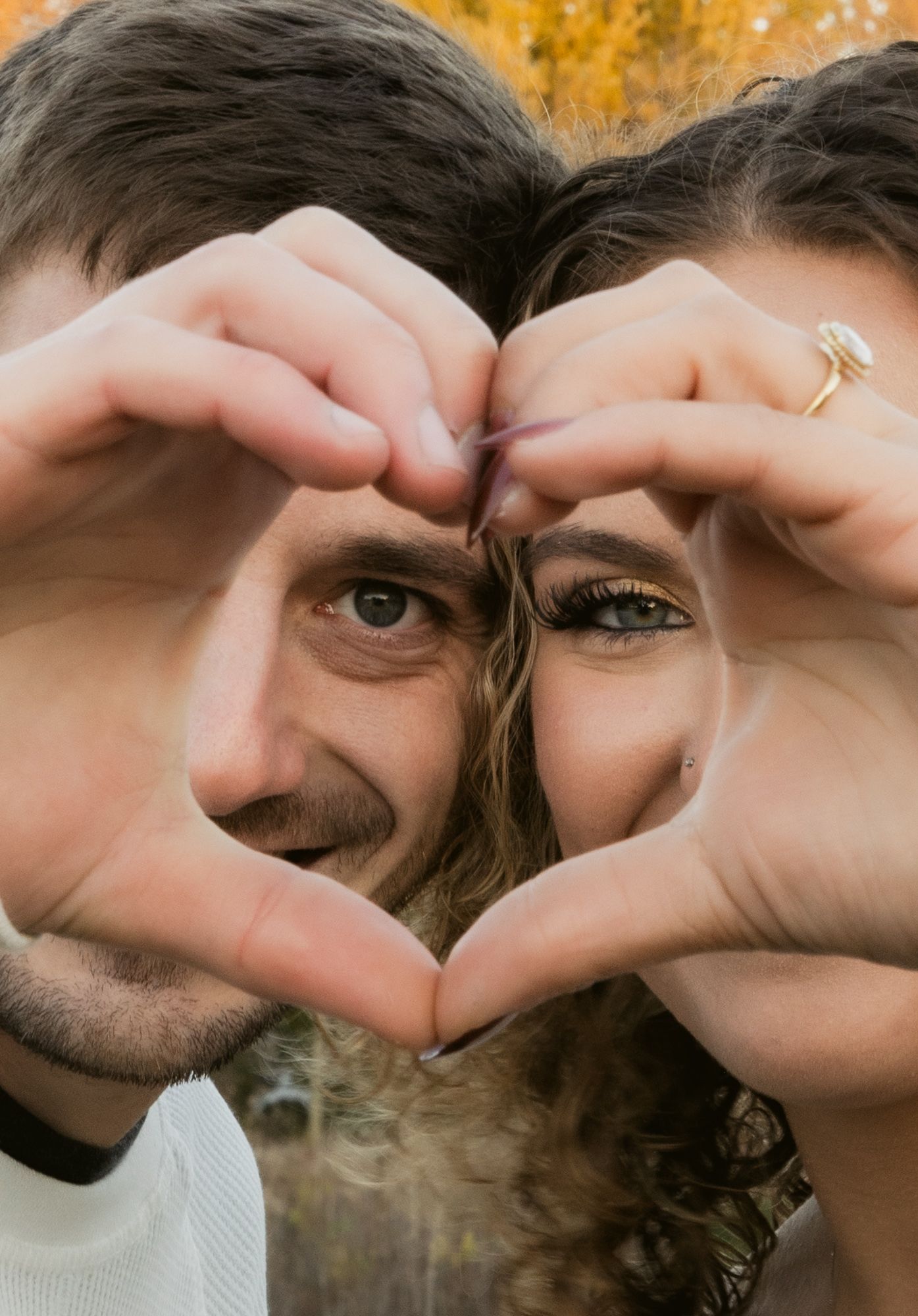A series of photos showing someone making heart shapes with their hands against a warm autumn background.