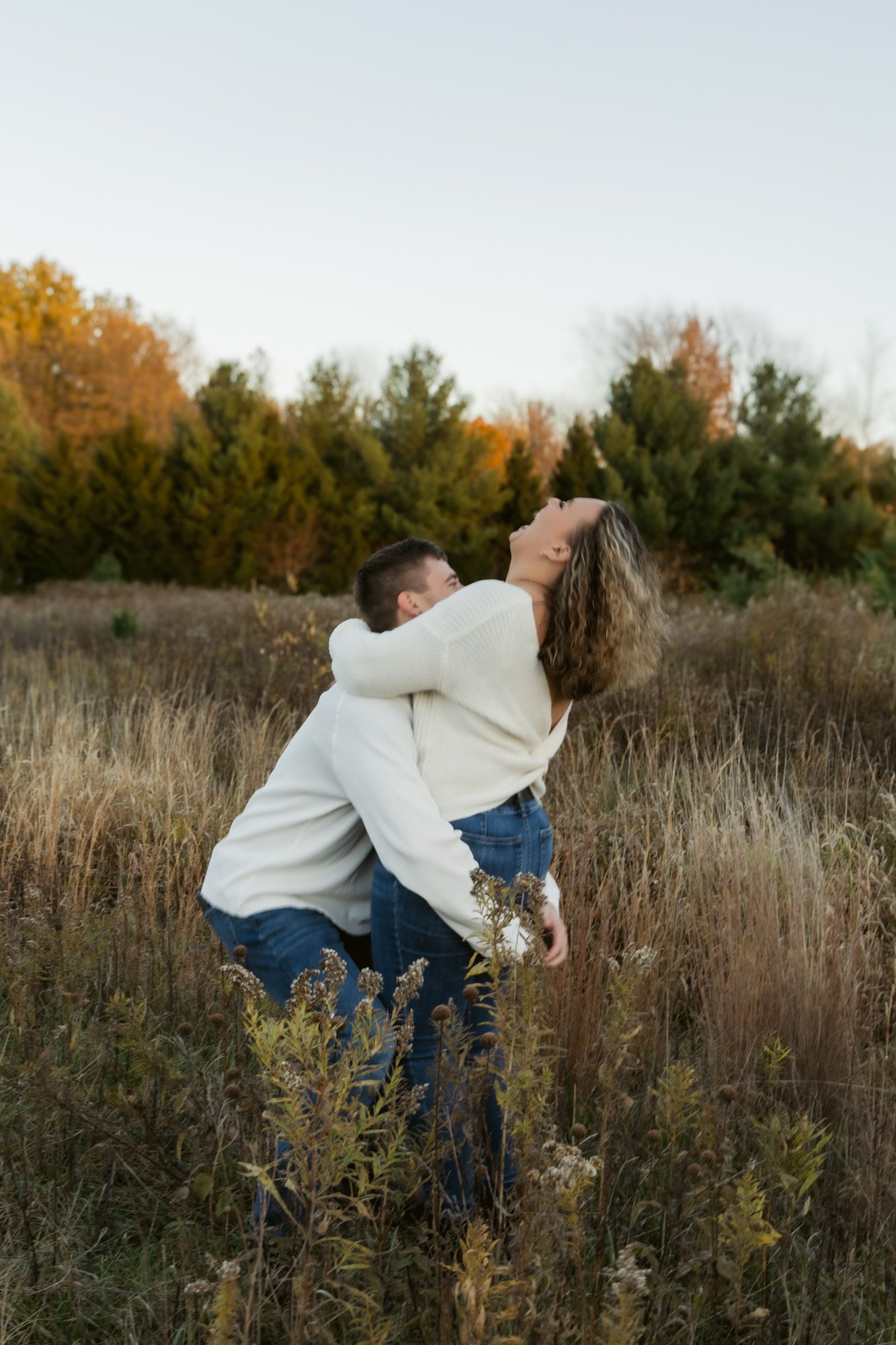 A person in a white sweater dances expressively through a field of tall grass during autumn.