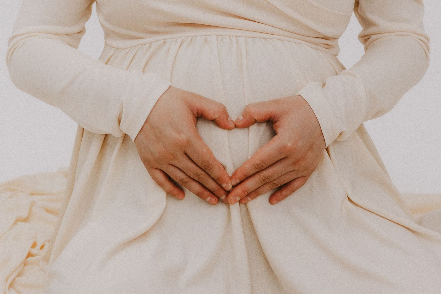 Hands forming a heart shape over a cream-colored dress.