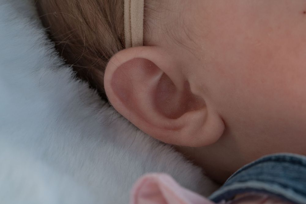 Close-up macro shot of a baby's ear and brown hair.