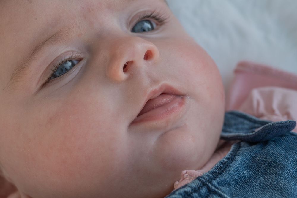 Close-up of a baby's face with bright blue eyes and rosy cheeks wearing denim.