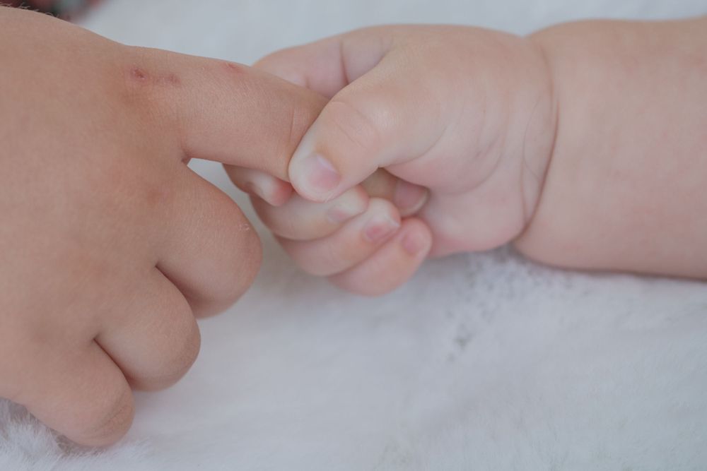 Two tiny hands tenderly touching each other against a white background.