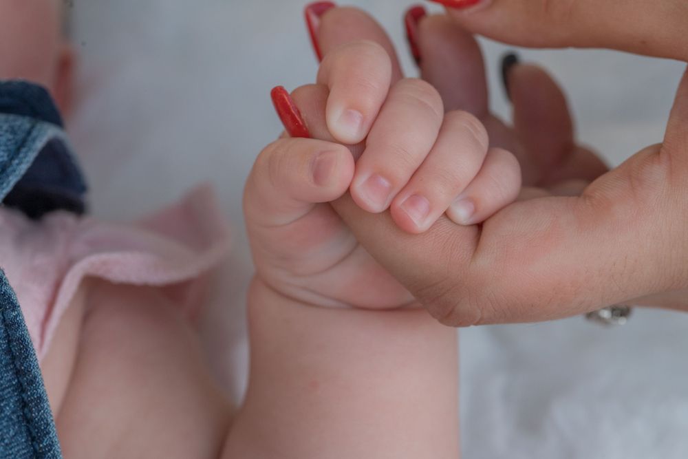Close-up of small baby hands being held by adult hands.