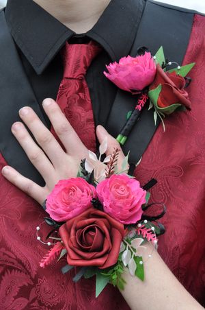 Pink and red floral corsages with roses displayed on a dark fabric background.