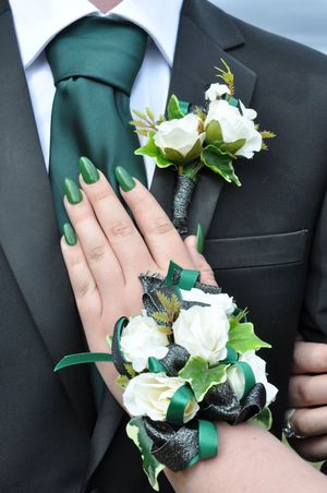 White rose corsage with green ribbon detail pinned to formal black suit.