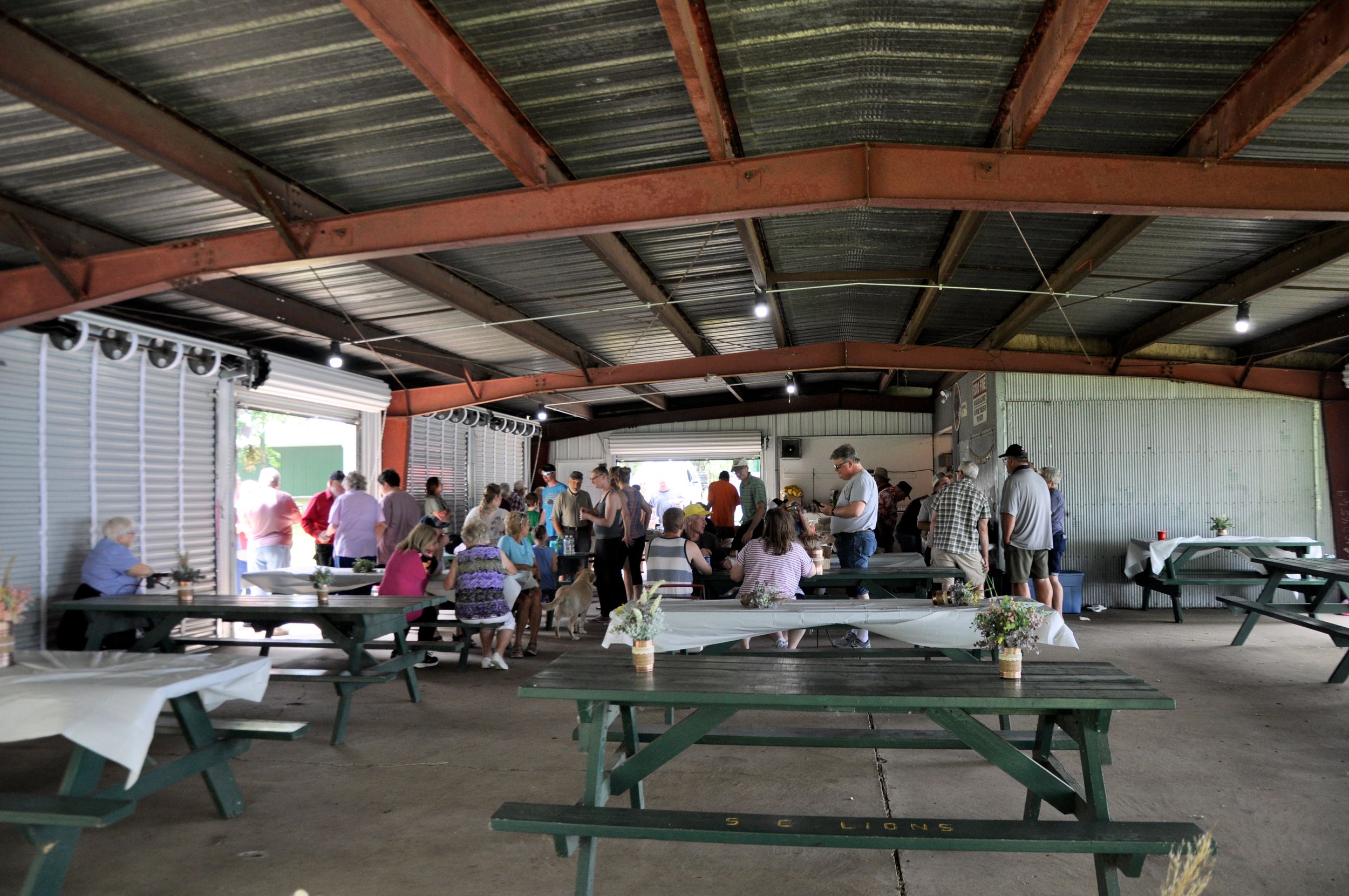 Wide view of a covered outdoor pavilion with green picnic tables and metal roof.