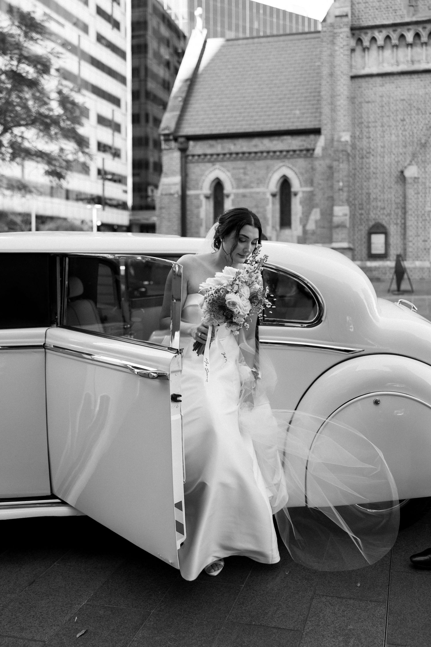 A sequence of black and white photos showing someone entering a classic white vintage car outside a church after a wedding.