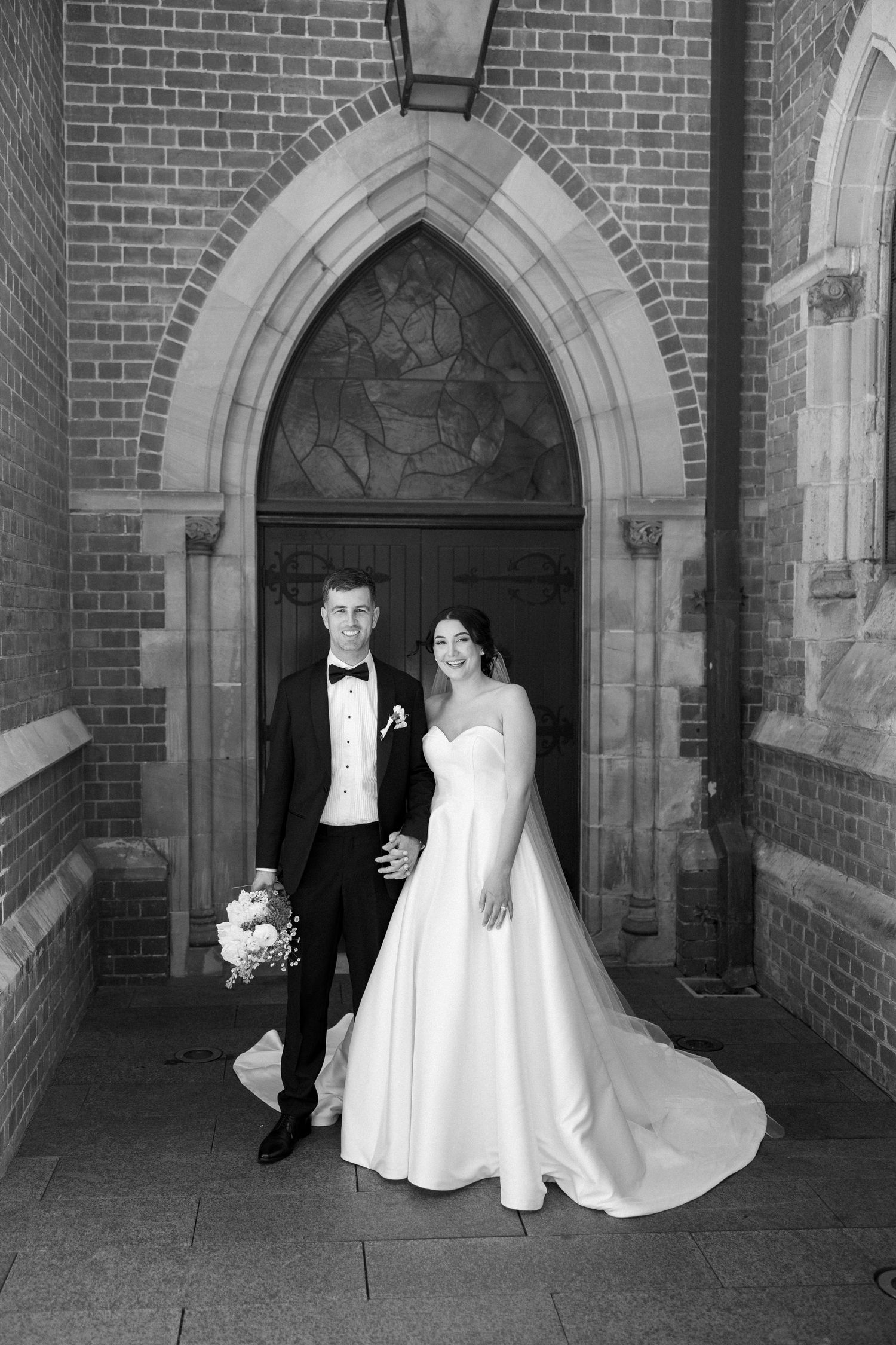 A couple in formal wedding attire poses together in a series of black and white photos under gothic stone archways.