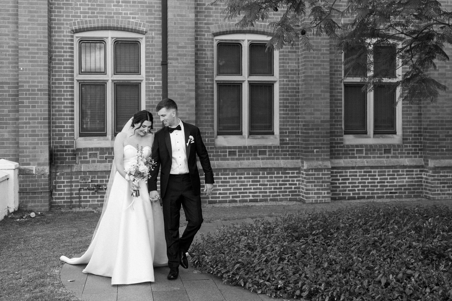 A black and white wedding photo sequence shows a couple walking together outside a brick building with classic architecture.