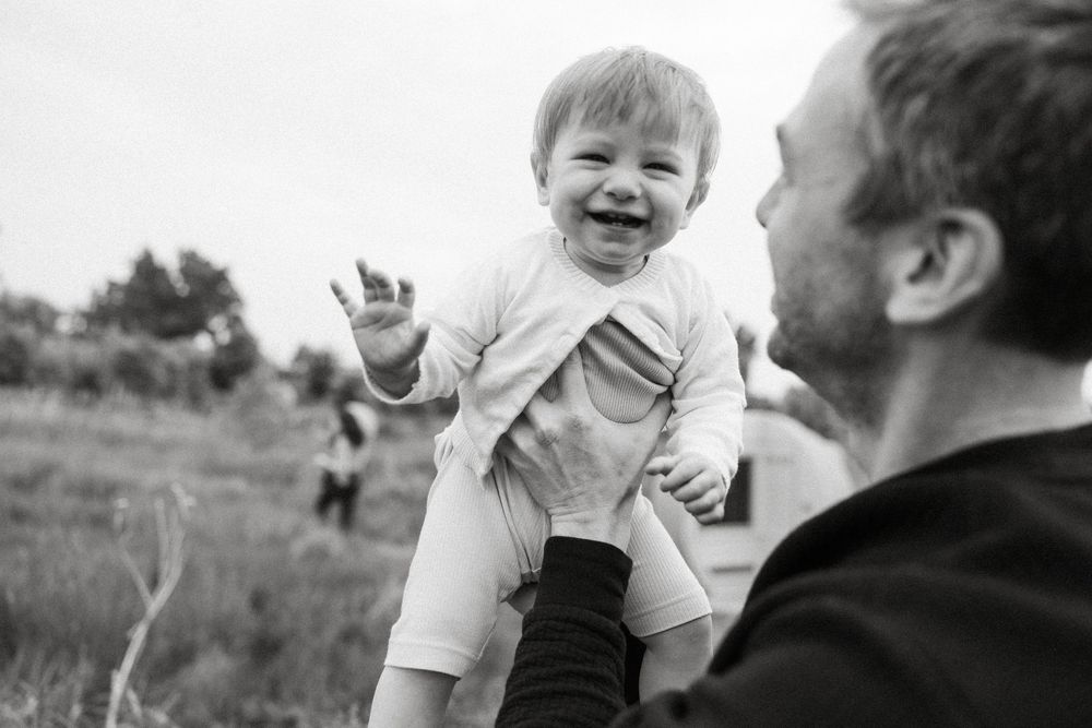 A series of black and white photos showing joyful moments between a parent and child playing together outdoors.