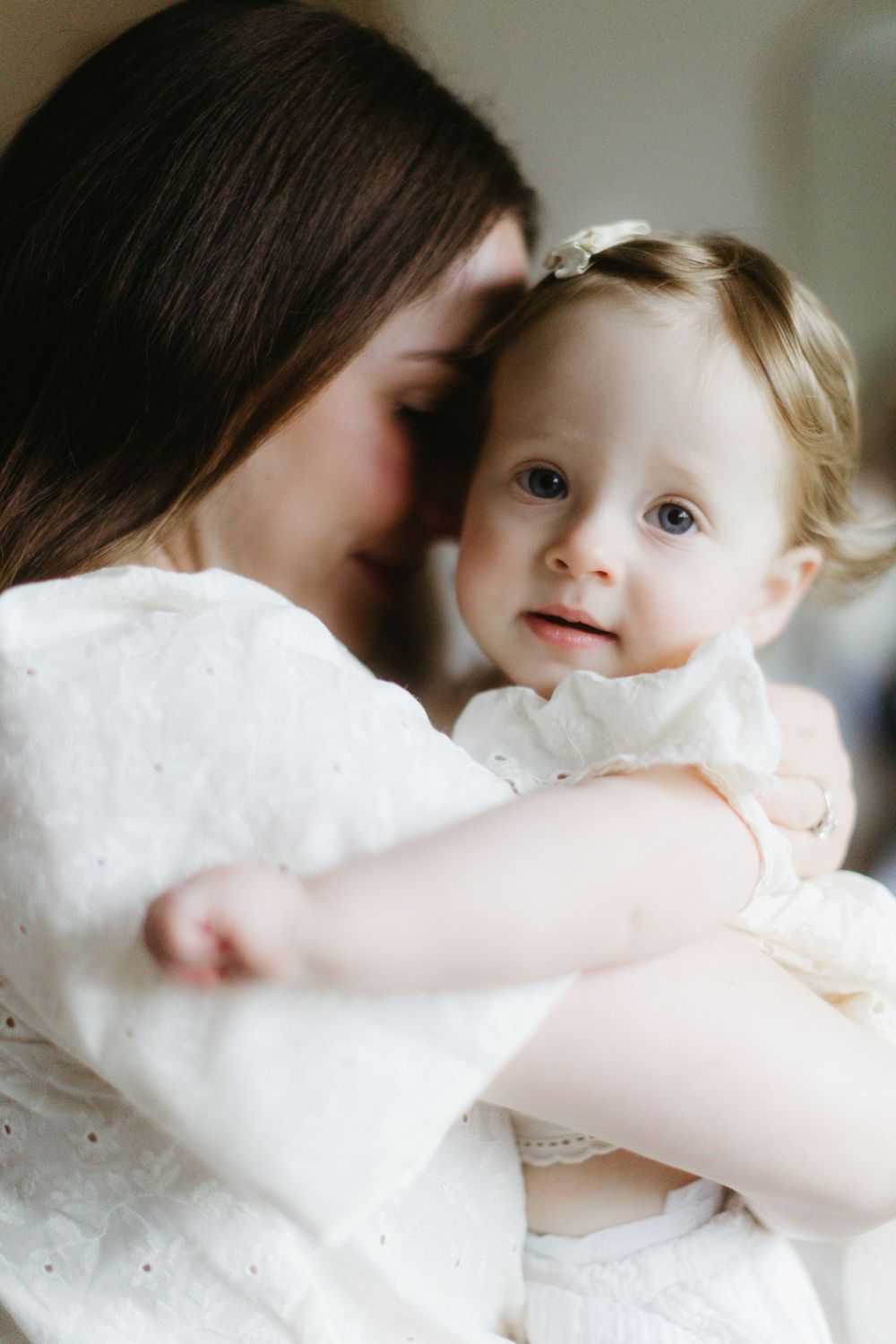 Tender moment captured between parent and baby in white attire showing affection and bonding.