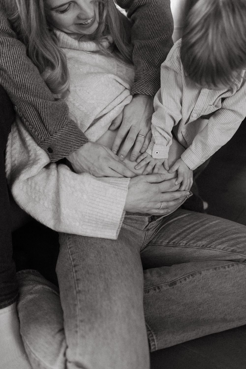 Black and white intimate photo showing hands lovingly placed on a pregnant belly, wearing casual sweater and jeans.