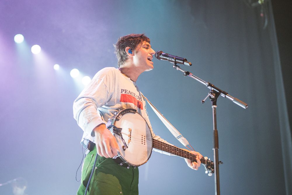 Musician performing with acoustic guitar on stage under blue and purple lighting.