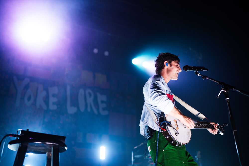 Musicians performing on stage with dramatic purple and blue concert lighting.