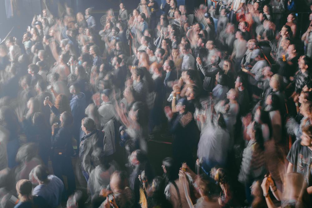 Enthusiastic concert crowd with raised hands enjoying a live performance in a dark venue.