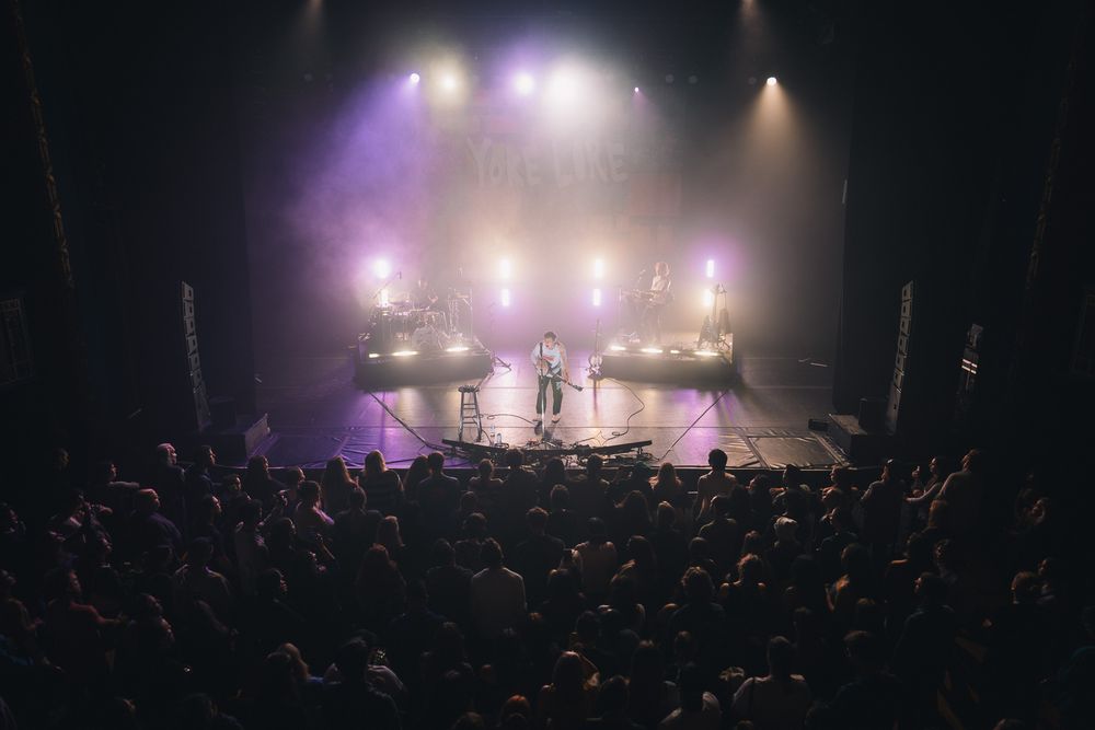 Concert venue filled with crowd silhouettes watching performers on illuminated stage.
