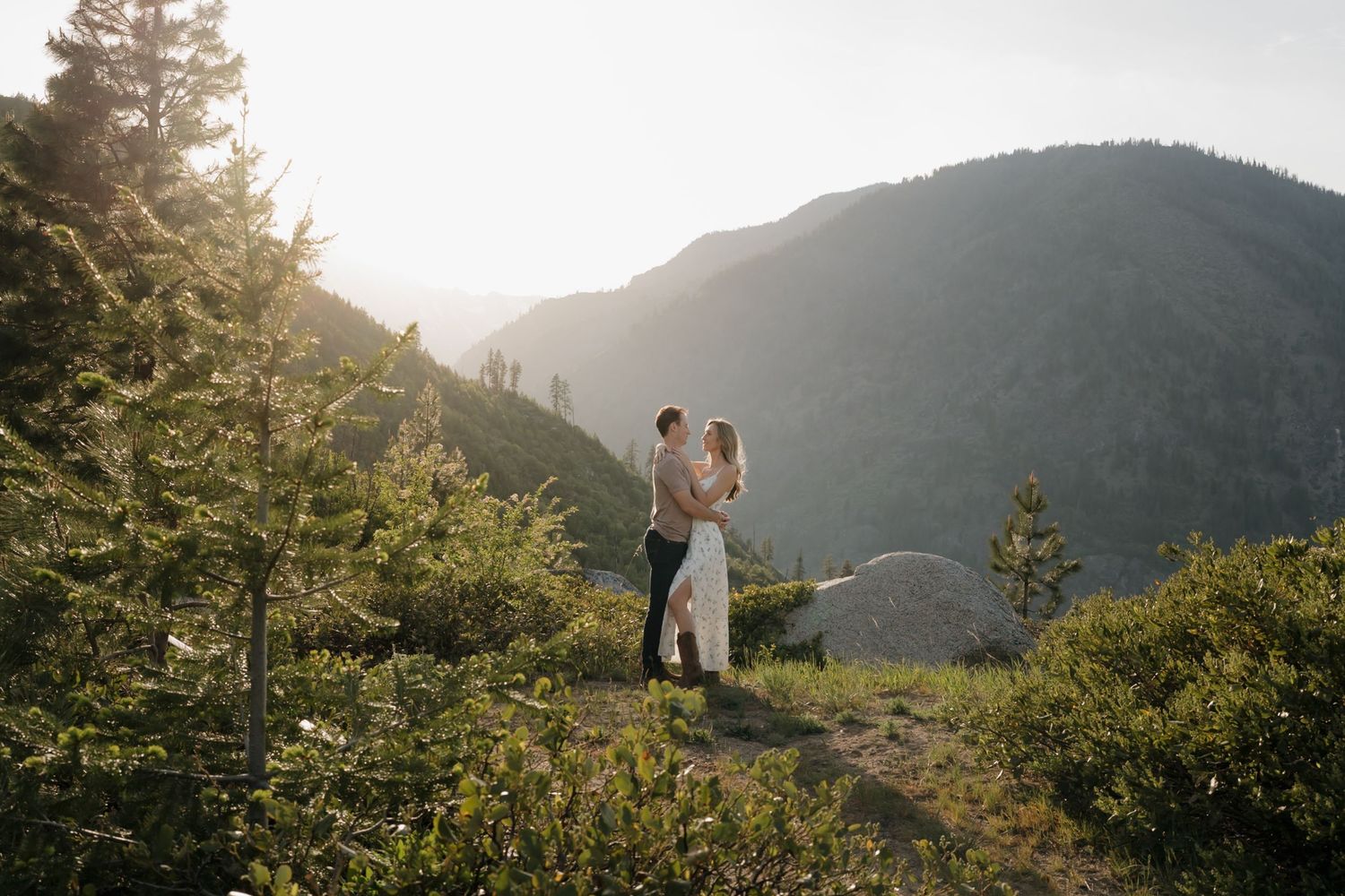 A joyful embrace between a couple in winter formal wear with snow-covered pine trees in background.