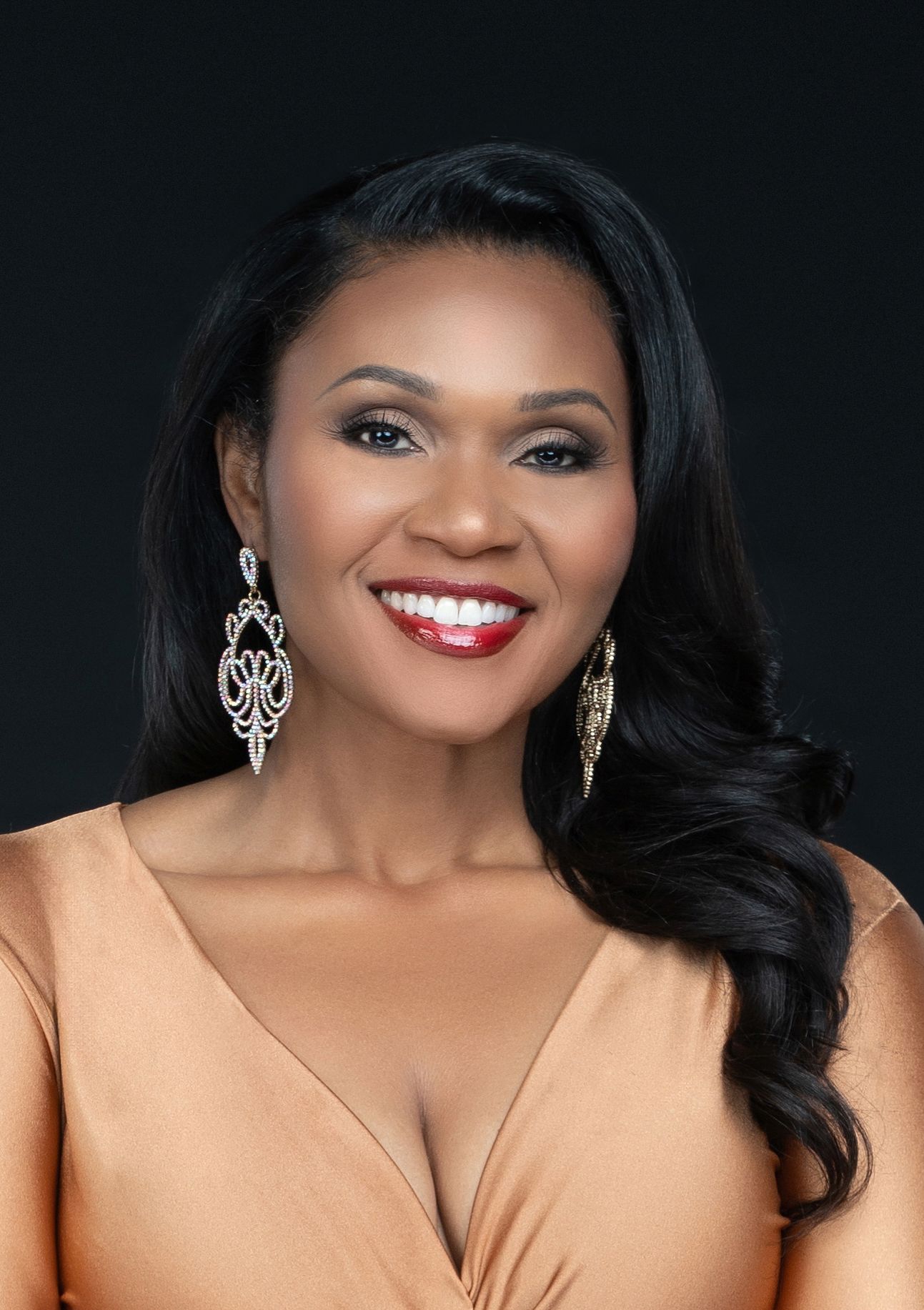 Glamorous portrait of person in peach dress with statement earrings against dark background.