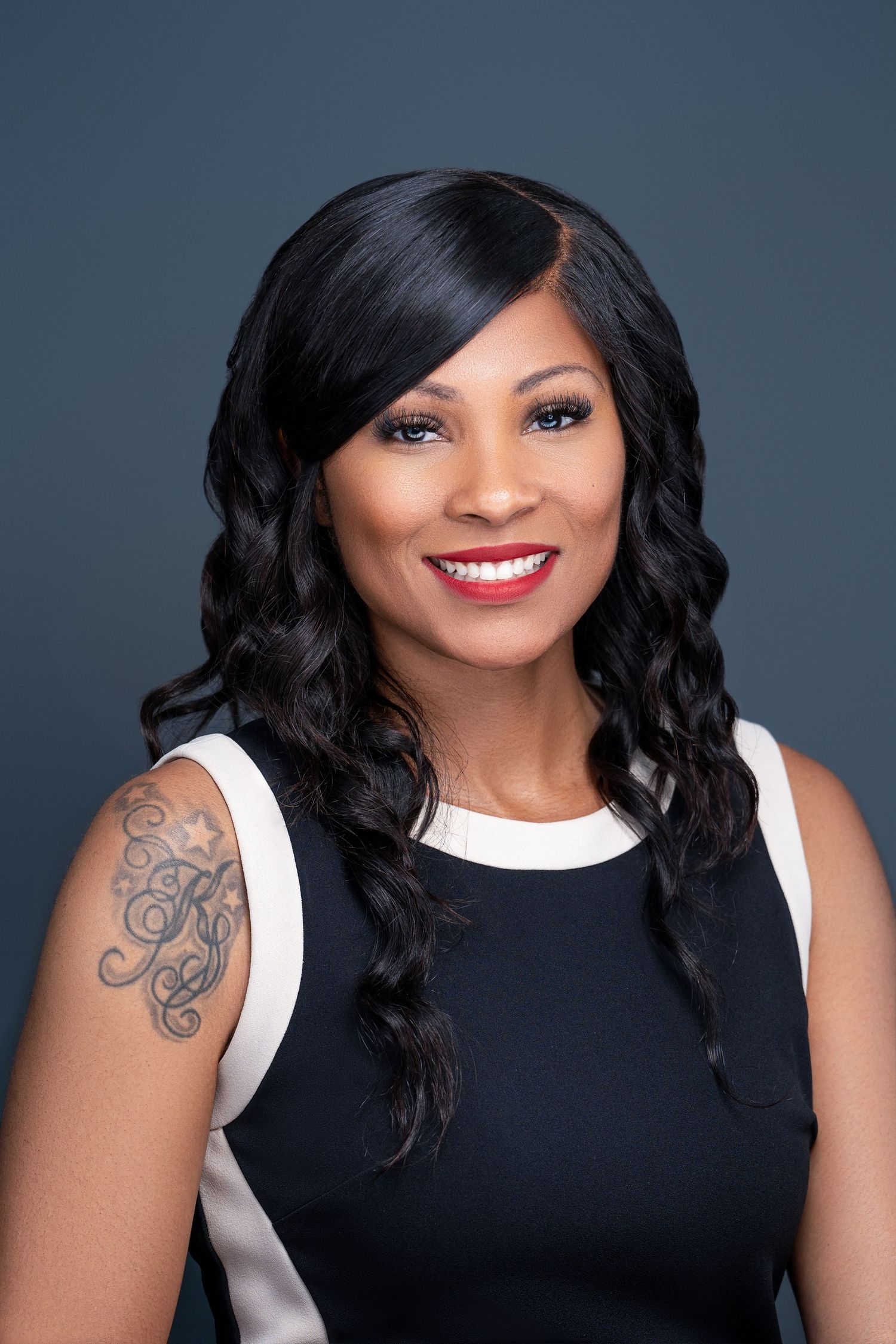 Studio portrait of person in black and white sleeveless top with visible arm tattoo.