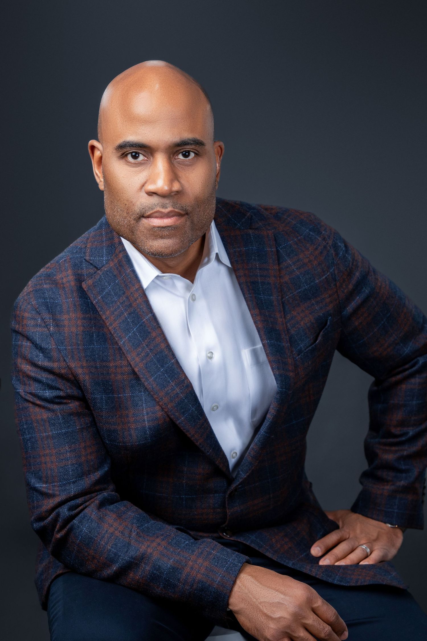 Professional headshot of person in plaid blazer against dark background.