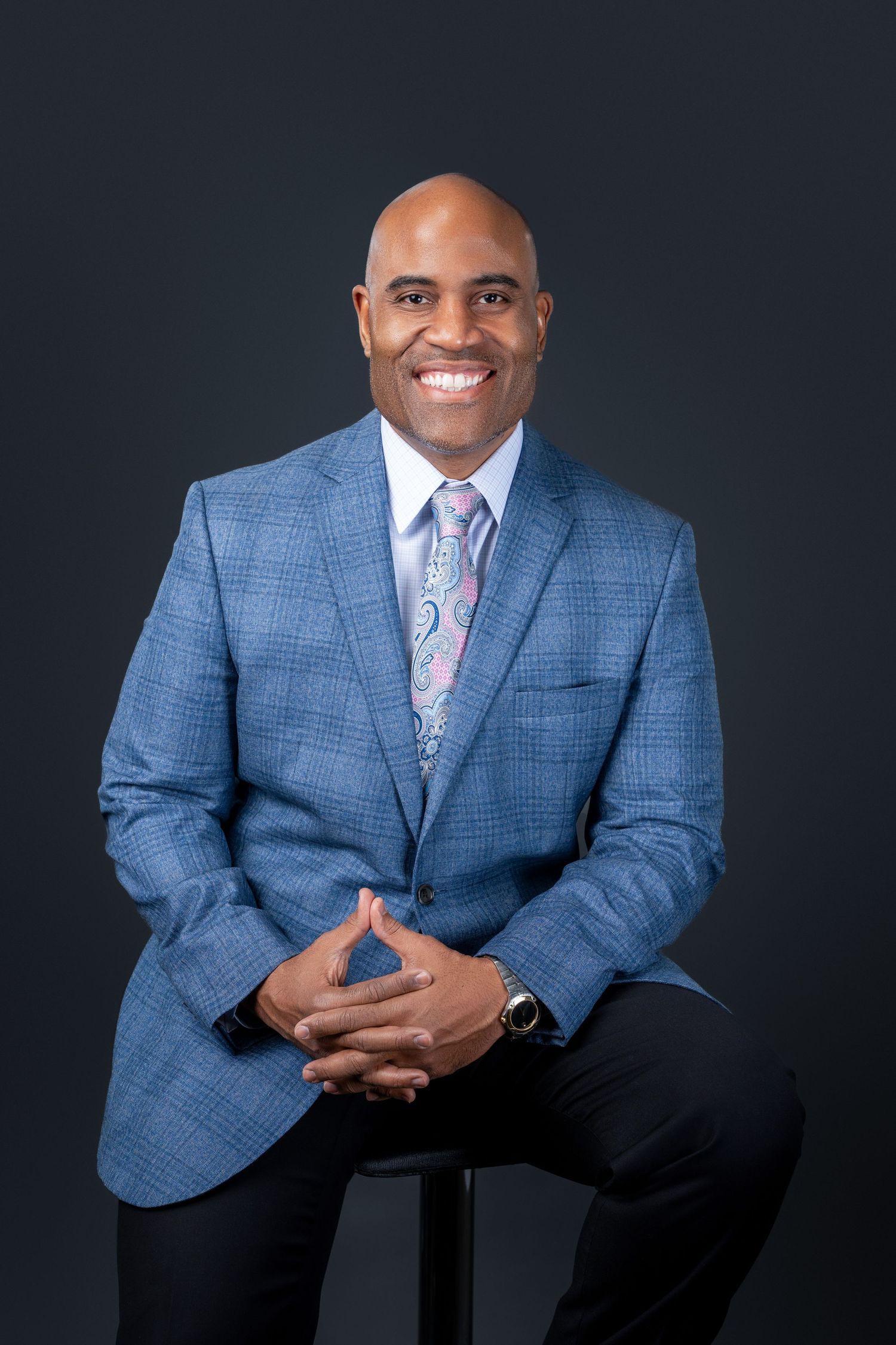 Professional portrait of person in blue plaid suit jacket and patterned tie.