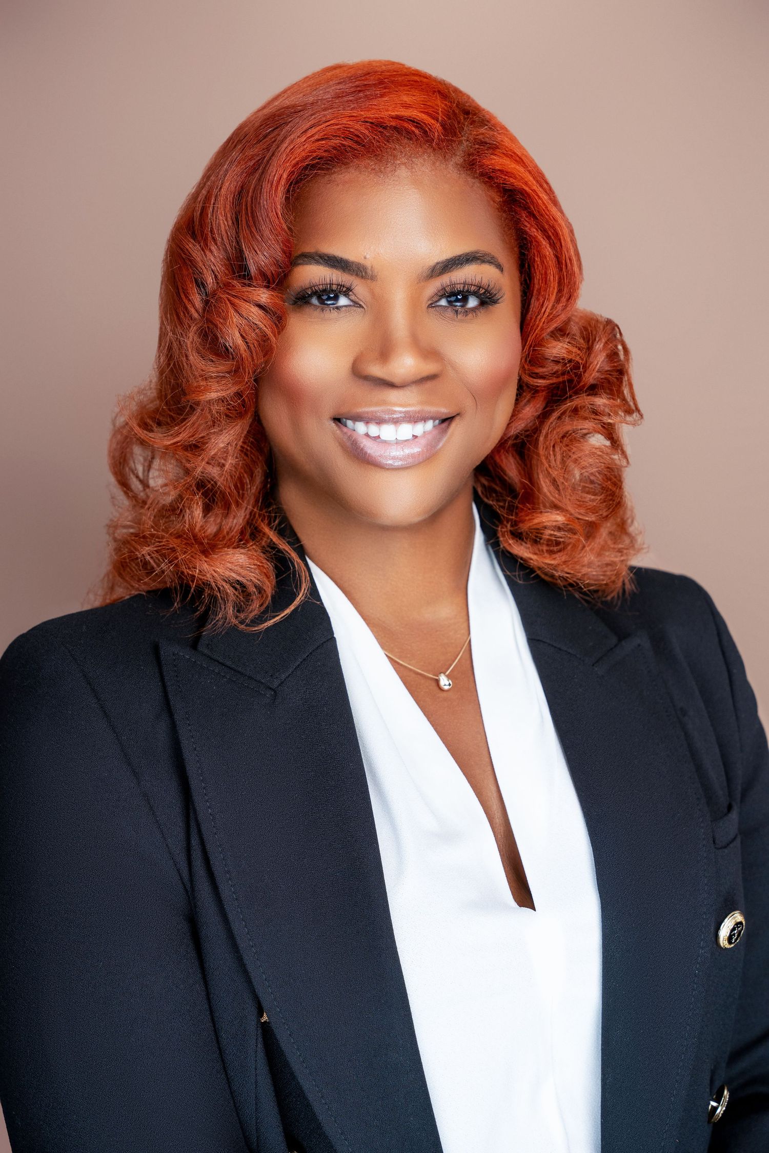 Professional headshot with styled auburn hair wearing classic black blazer and white top.